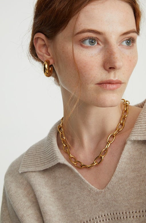 a white woman wearing a thick chunky gold c hoops and chunky statement chain necklace with her hair up-do.
